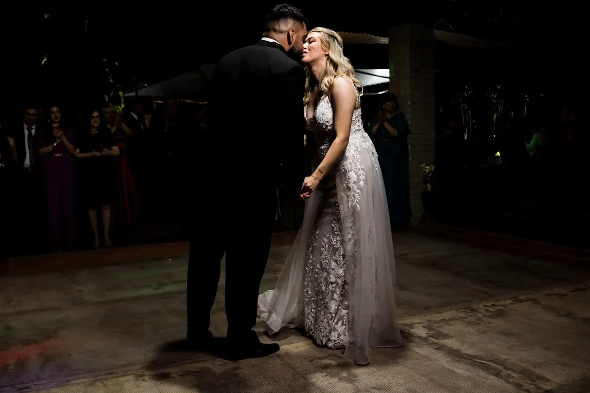 Beso de los novios durante el primer baile, invitados mirando