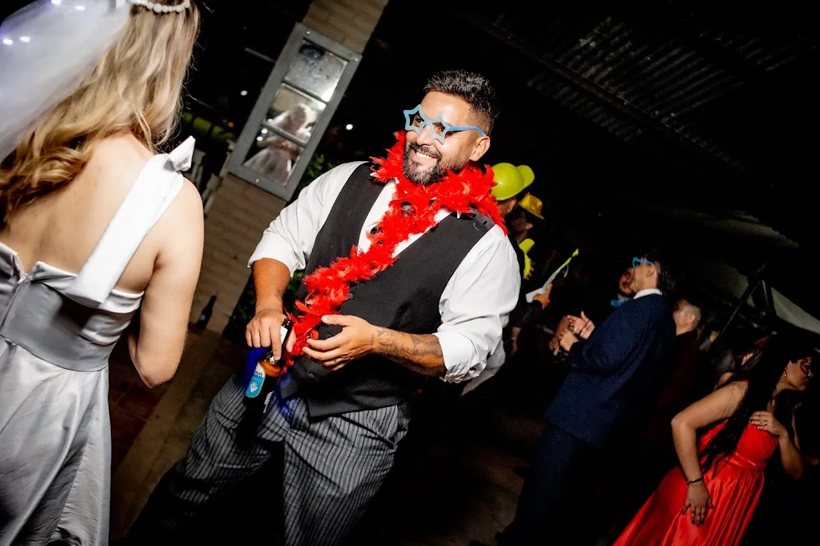 El novio con boa de plumas roja, riendo en la fiesta