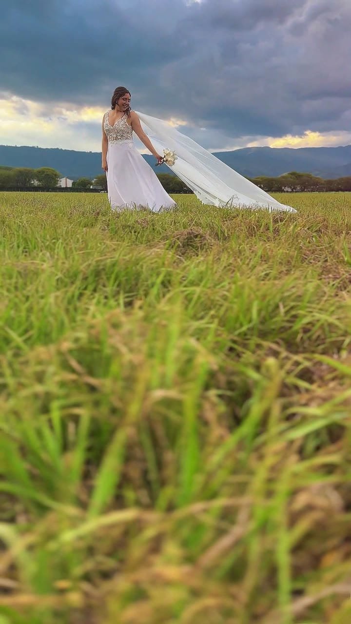 Novia con el velo flameando al viento en un campo al atardecer