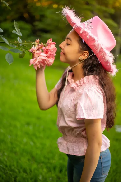 Sombrero rosa con plumas, oliendo una rosa
